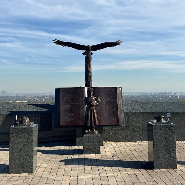A memorial with an eagle, a book-shaped plaque, and a statue of a girl, overlooking a city.