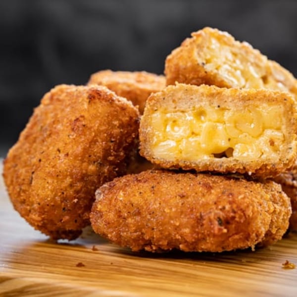 Golden-brown, crispy fried mac and cheese bites, one cut open to show creamy pasta inside.