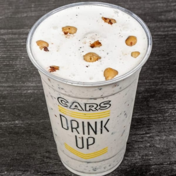 A CARS Eatery milkshake, topped with cookie pieces, sits on a dark wooden surface.