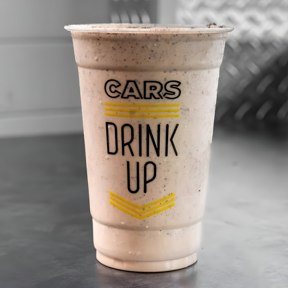 A CARS Eatery cookies and cream milkshake in a clear plastic cup with "DRINK UP" text.