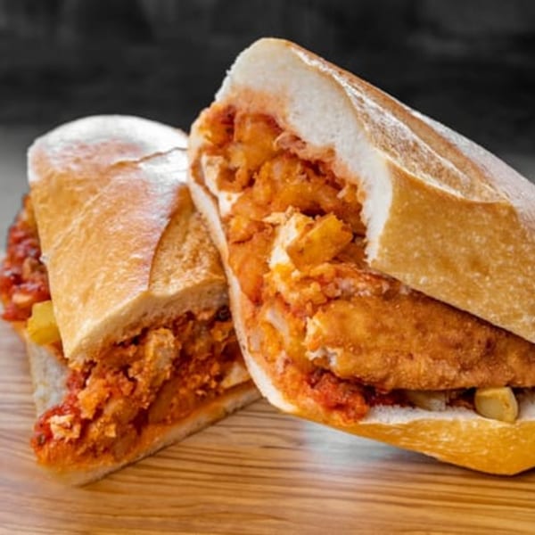 Two halves of a crispy chicken sandwich with red sauce and fries on a wooden board.