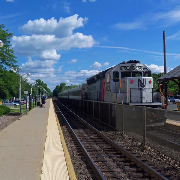 A train with "NJ Transit" on its front sits at a station platform under a blue sky.