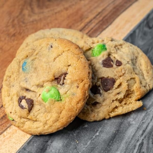 Two CARS Eatery chocolate chip cookies with green and blue candies on a wooden and marble surface.