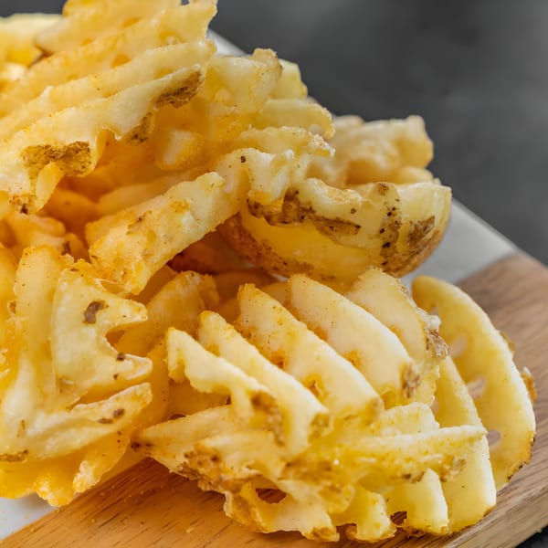 Close-up of golden-brown waffle fries seasoned with spices, on a wooden board.