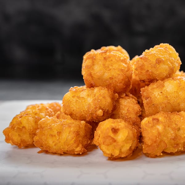 A close-up of a pile of golden-brown, crispy tater tots on a white surface.