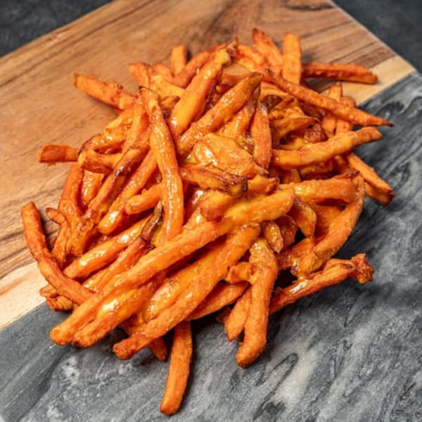 A pile of golden-brown sweet potato fries on a wooden and dark grey cutting board.