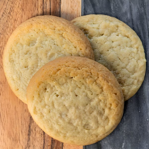 Three golden-brown sugar cookies arranged on a split wooden and dark gray surface.