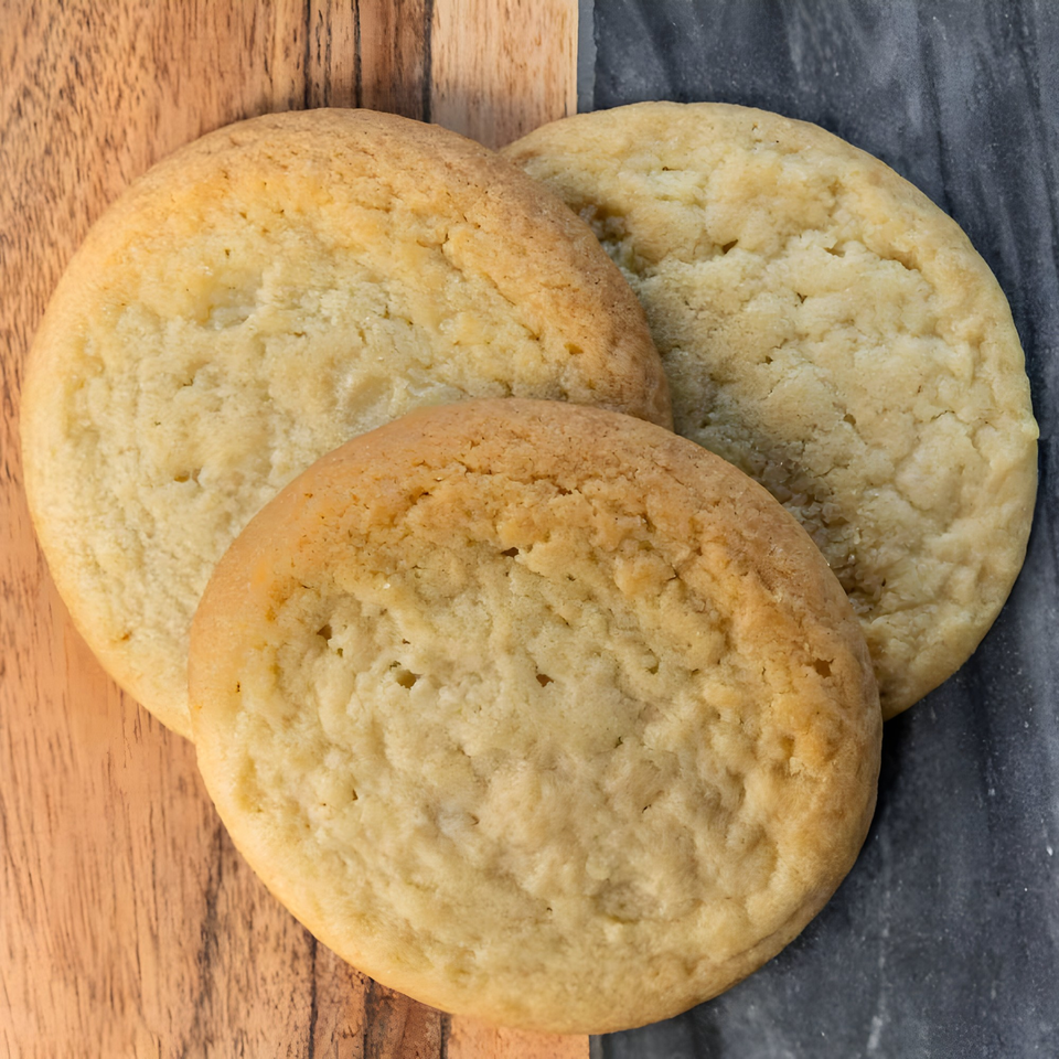 Three golden-brown sugar cookies arranged on a split wooden and dark gray surface.