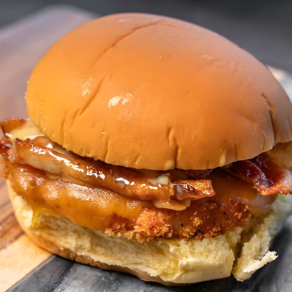 A close-up of a CARS Eatery fast-food sandwich with crispy chicken, bacon, and melted cheese.