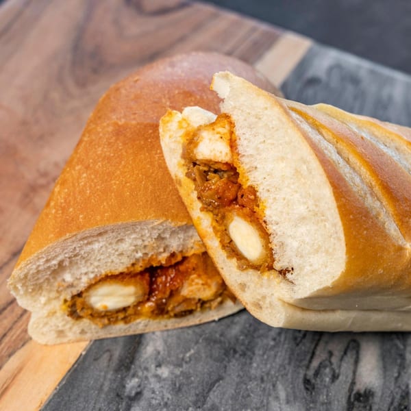 Two halves of a CARS Eatery chicken sandwich with melted cheese and sauce on a wooden board.