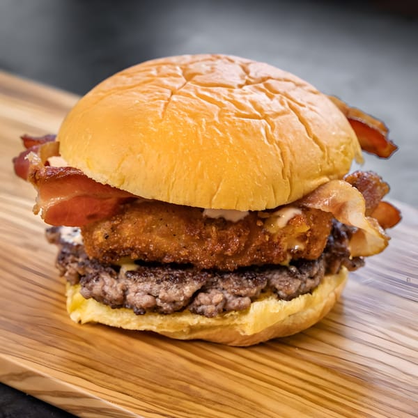 CARS Eatery's fast-food burger with bacon, a fried patty, and a beef patty on a bun.