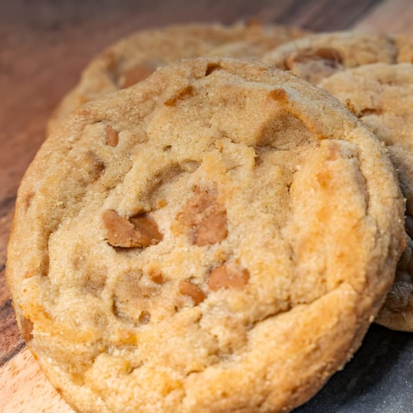 Close-up of a golden-brown cookie with visible butterscotch chips, on a wooden surface.