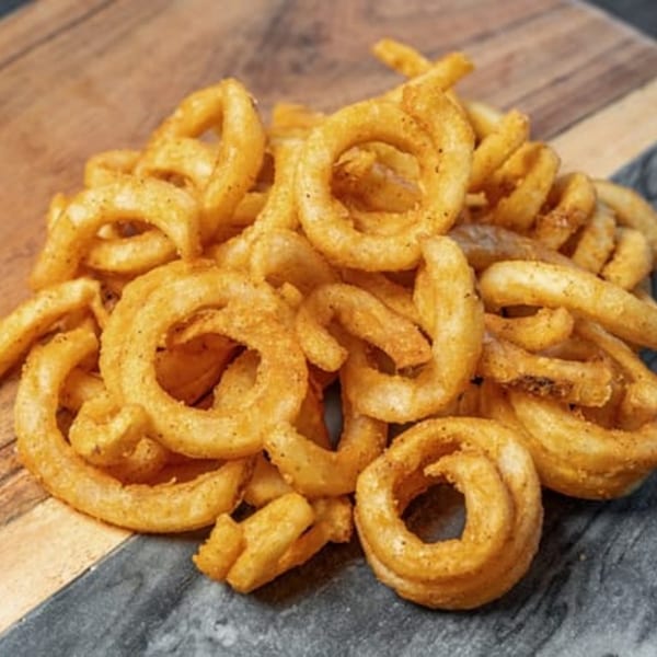 A pile of golden-brown, seasoned curly fries from CARS Eatery on a wooden and dark gray surface.