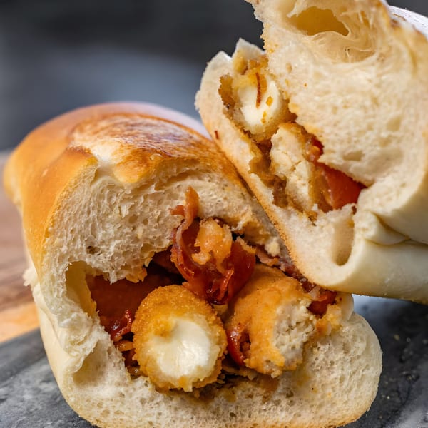 A close-up of a CARS Eatery fast-food sandwich, cut in half, revealing fried cheese and bacon.