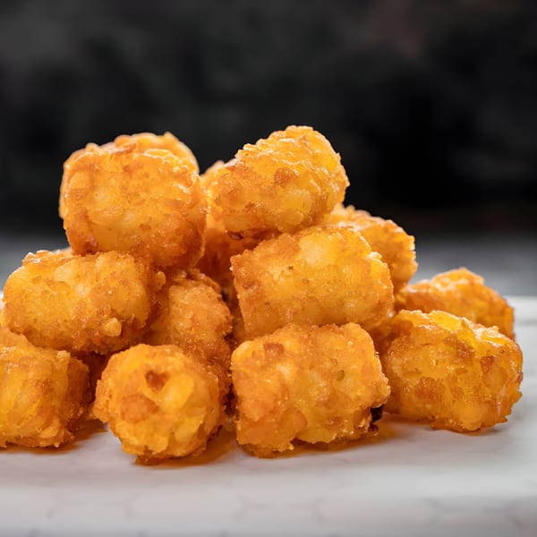 A close-up of a pile of golden-brown, crispy tater tots on a white surface.