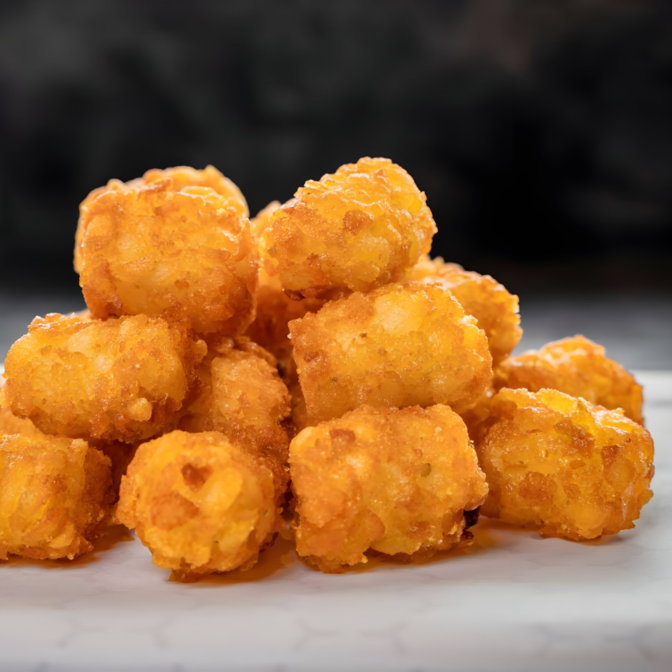 A close-up of a pile of golden-brown, crispy tater tots on a white surface.
