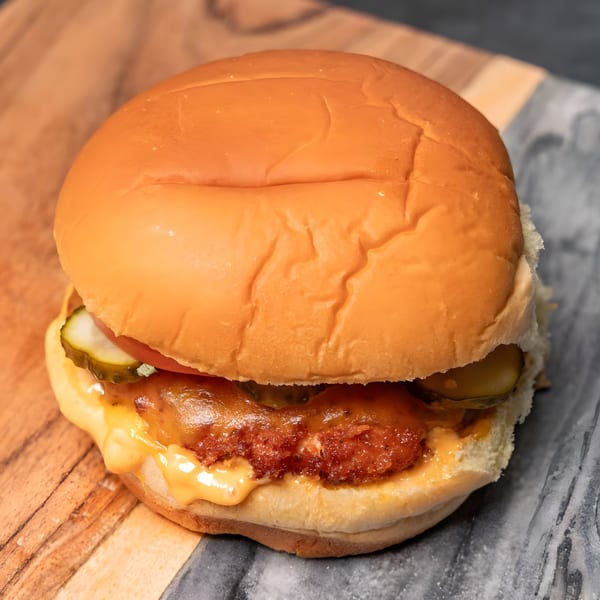 A CARS Eatery fast-food chicken sandwich with pickles, tomato, and cheese on a bun.
