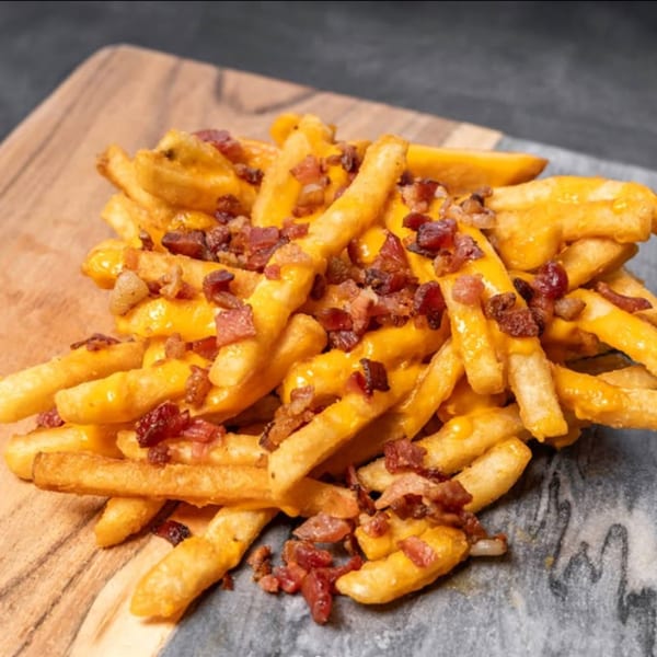Golden french fries covered in melted cheese and crispy bacon bits on a wooden and stone board.