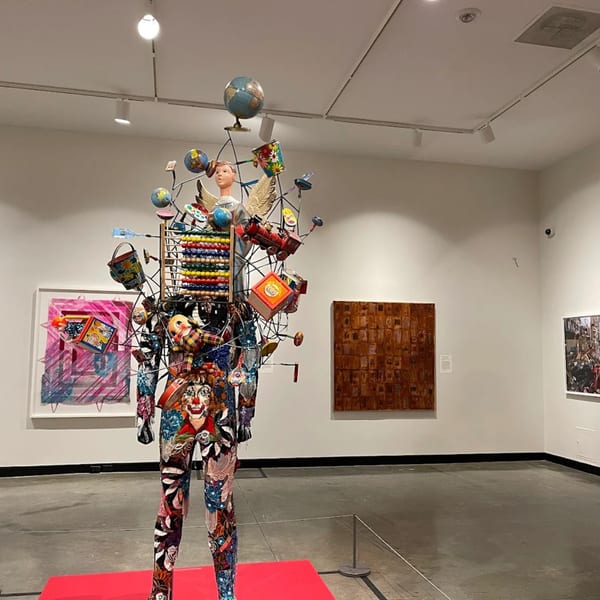 A colorful, human-shaped sculpture adorned with various objects, including globes, toys, and an abacus.