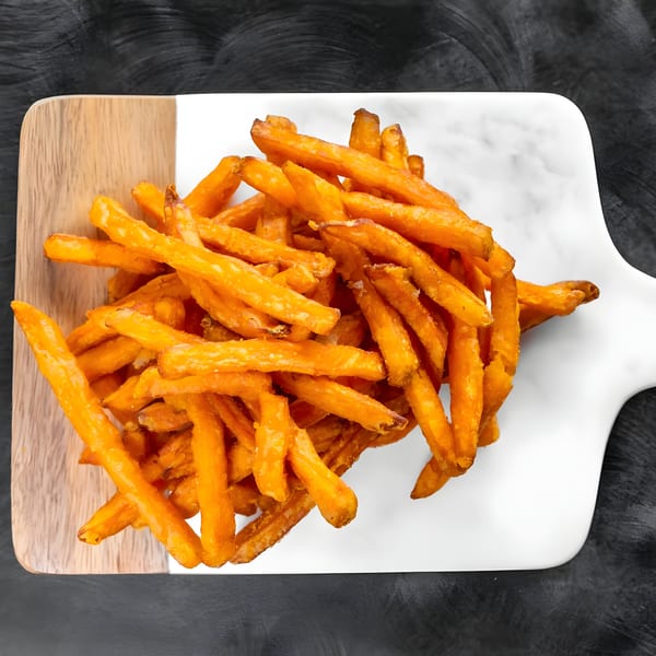A pile of golden-orange sweet potato fries on a white and wood serving board.