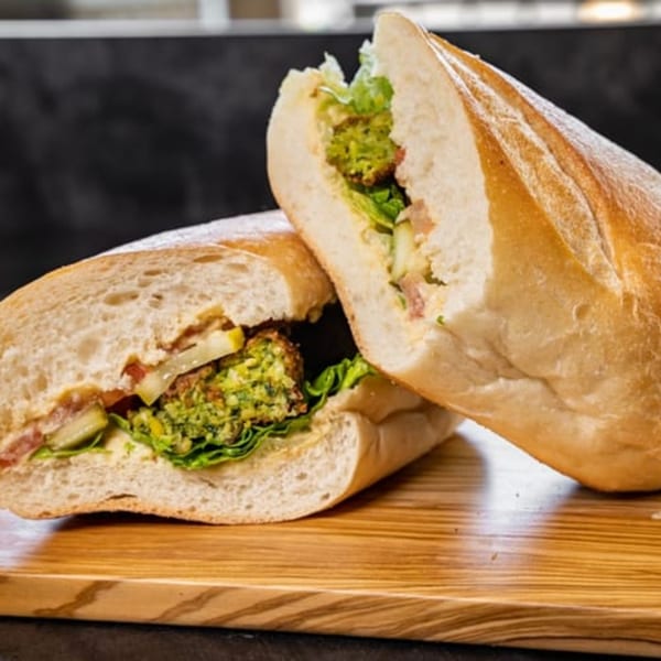 A falafel sandwich from CARS Eatery, cut in half, revealing green falafel, lettuce, and sauce.