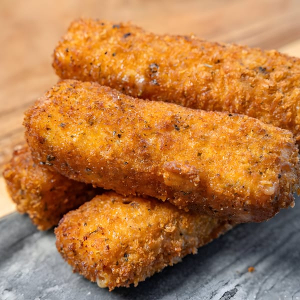 Close-up of golden-brown, breaded mozzarella sticks seasoned with herbs, stacked on a dark surface.