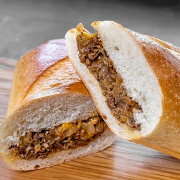 Two halves of a CARS Eatery cheesesteak sandwich, filled with meat, onions, and melted cheese.