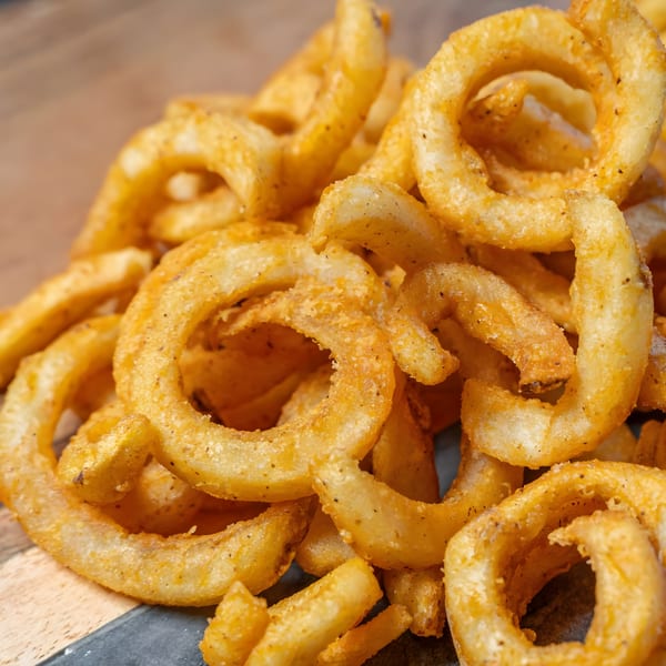 Close-up of a pile of golden, seasoned curly fries from CARS Eatery on a wooden surface.