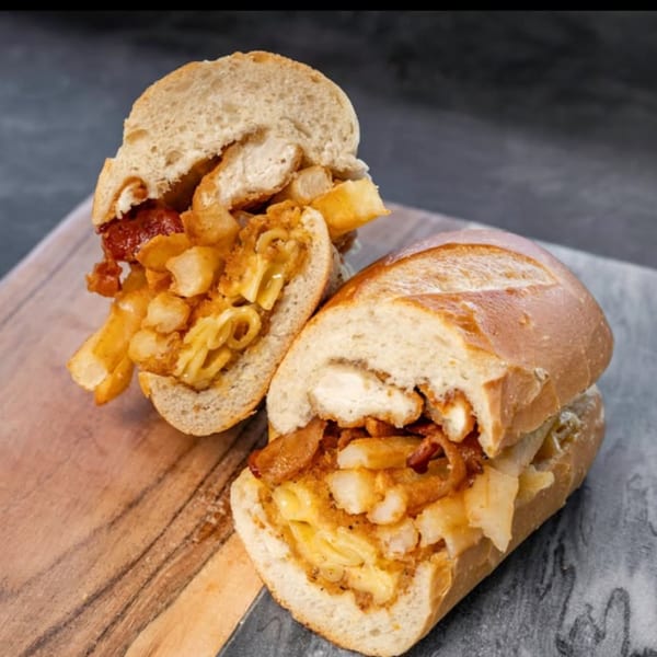 Two halves of a loaded CARS Eatery sandwich, overflowing with fries, mac and cheese, and chicken.