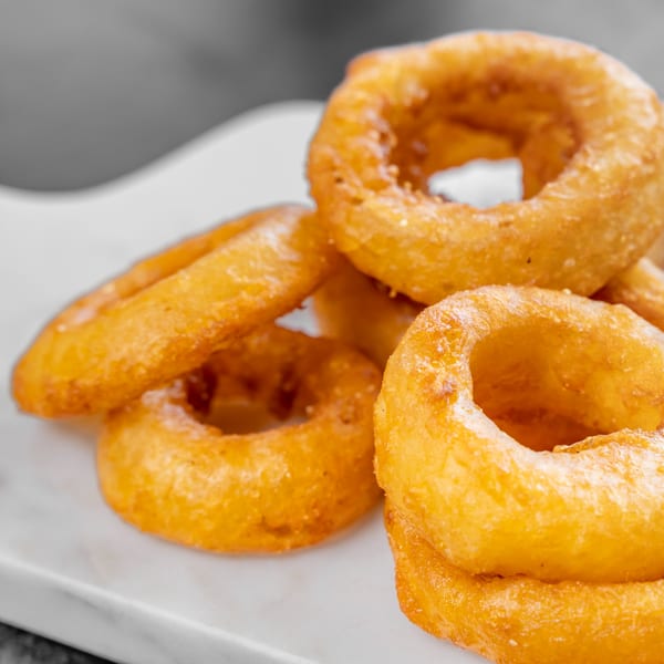 Golden-brown, crispy onion rings from CARS Eatery piled on a white serving dish.