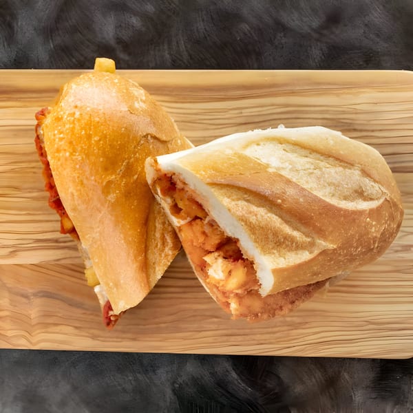 Two halves of a golden-brown sub sandwich, filled with chicken and sauce, on a wooden board.