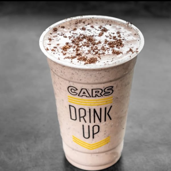 CARS Eatery's cookies and cream milkshake in a clear plastic cup with "DRINK UP" text.