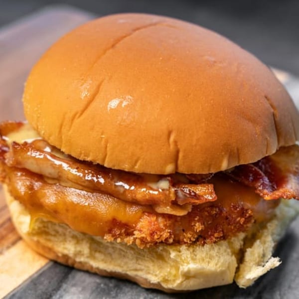 Close-up of a CARS Eatery fast-food sandwich with crispy chicken, bacon, and melted cheese.