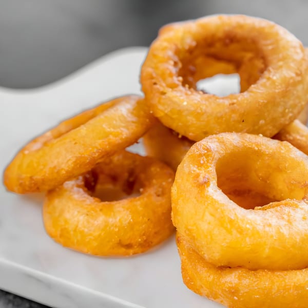 Close-up of golden-brown, crispy onion rings piled on a white serving dish.