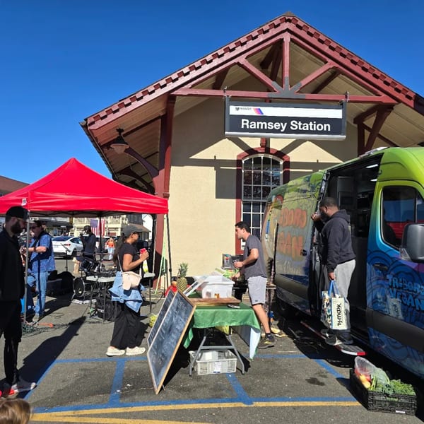 People gather around a food truck and red tent outside Ramsey Station on a sunny day.