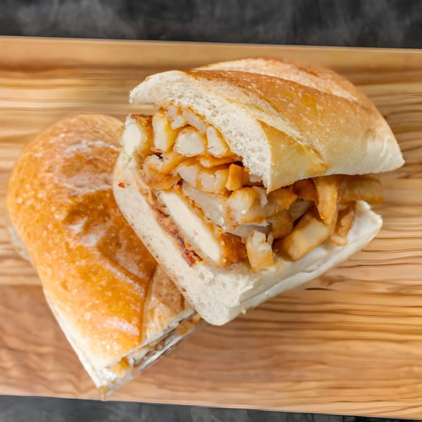 A CARS Eatery fast-food sandwich, filled with chicken and french fries, on a wooden tray.