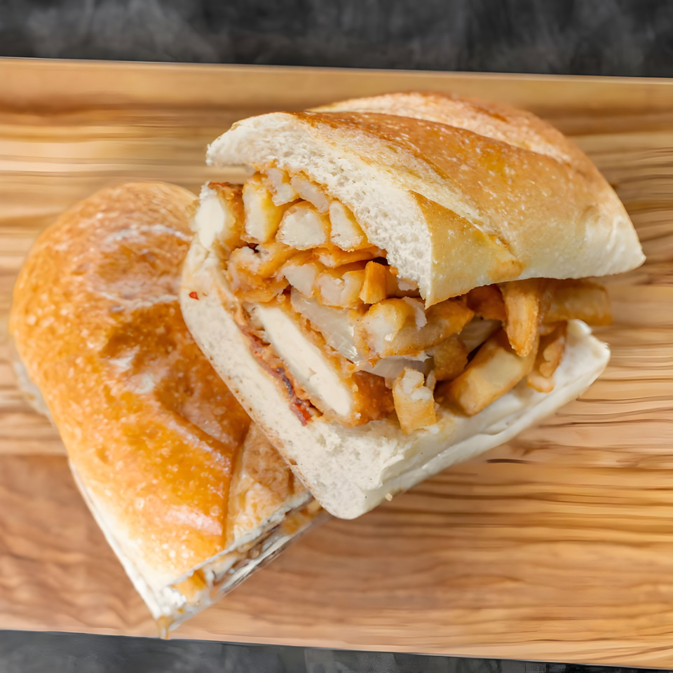 A CARS Eatery fast-food sandwich, filled with chicken and french fries, on a wooden tray.