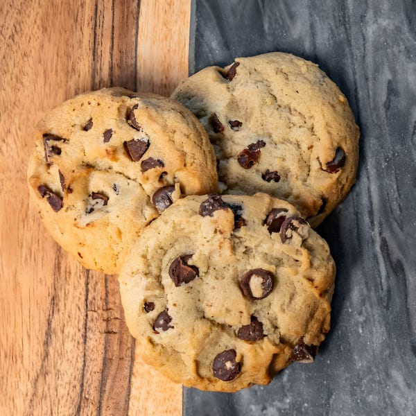 Three chocolate chip cookies on a wooden and dark gray surface.